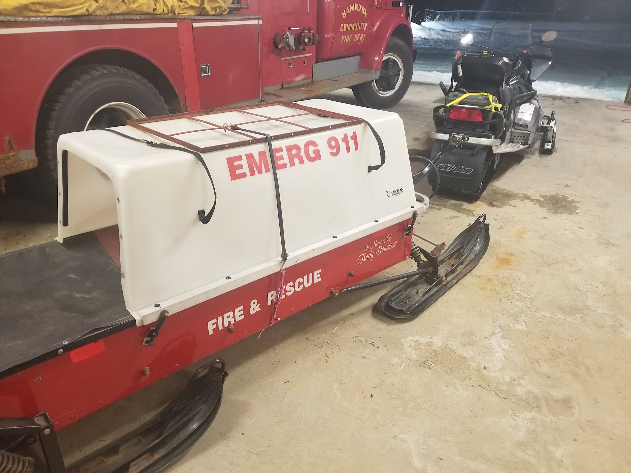 Rescue toboggan marked EMERG 911 Fire and Rescue hitched to a snowmobile