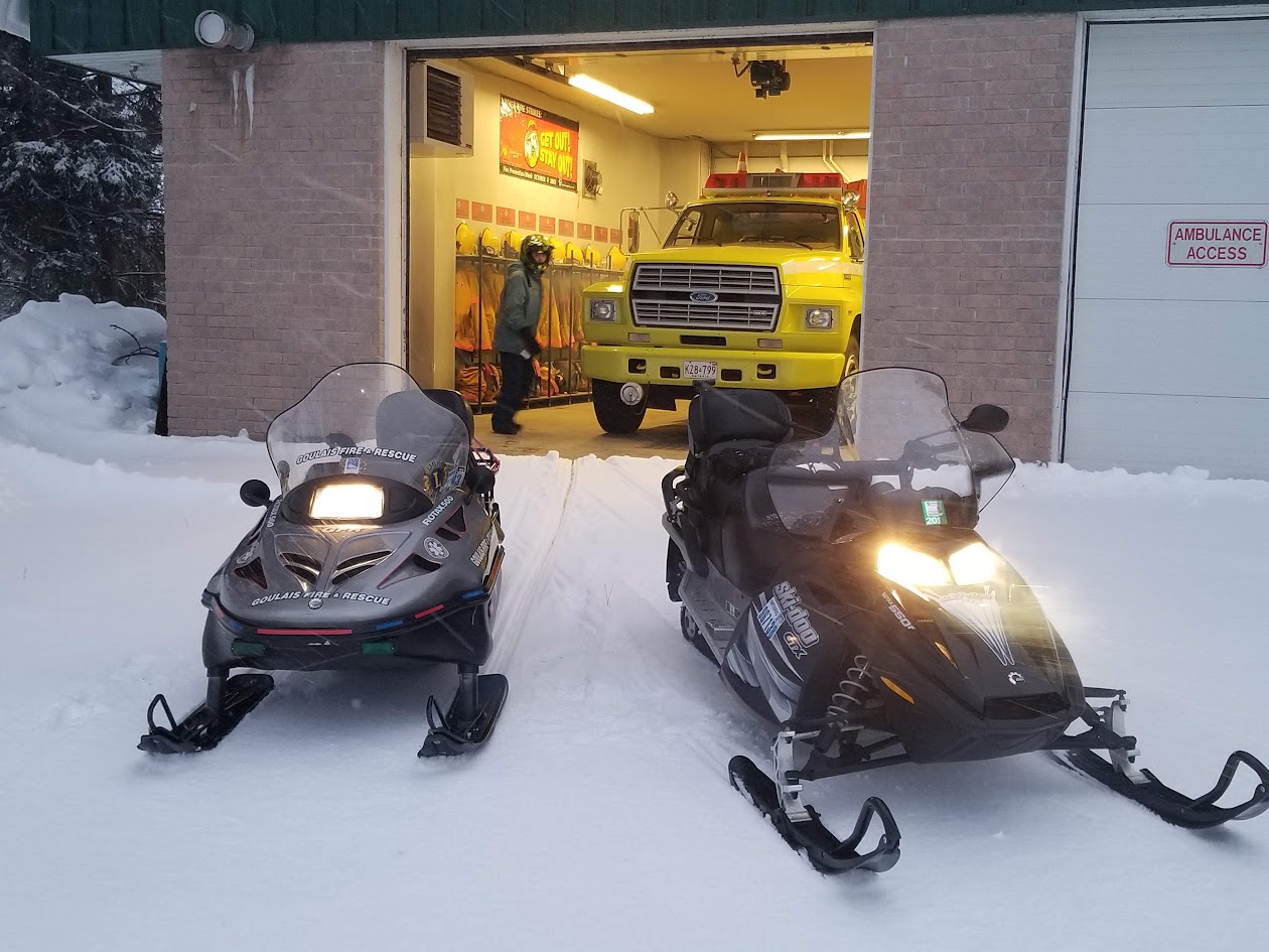 Two Goulais Fire and Rescue snowmobiles outside the open fire hall bay in winter